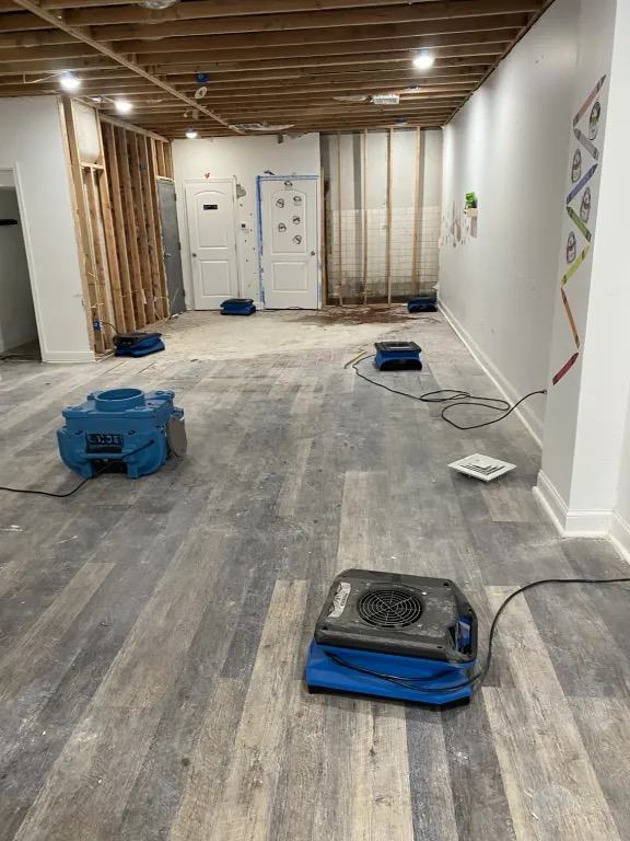 Room with the ceiling open to the joists and wall sections open to the studs, with blue air movers running on the floor.