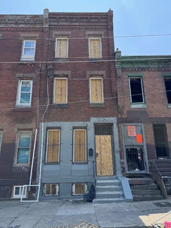 A brick rowhouse with plywood covering the windows and front door.