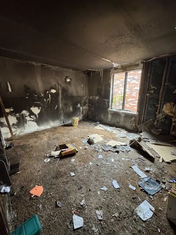 The room emptied of contents, with soot covered walls and ceiling and loose debris on the floor.