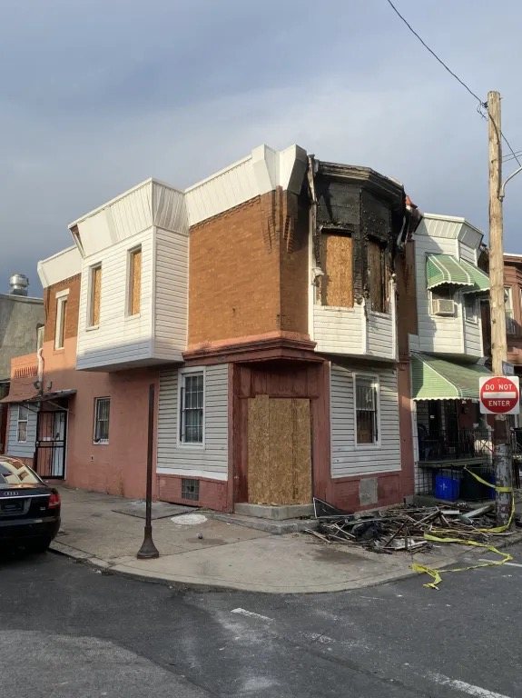 Corner house boarded up with plywood over the door and windows after a fire.