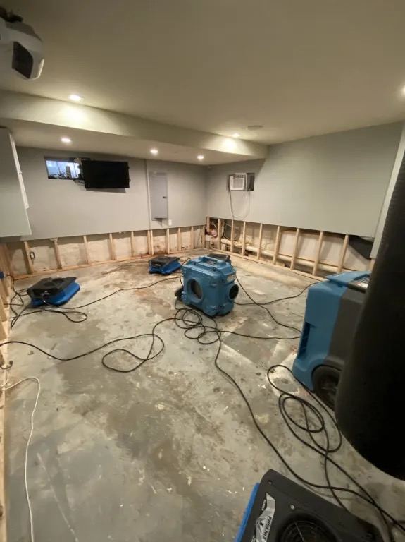 A basement room with the lower walls removed and drying equipment running.